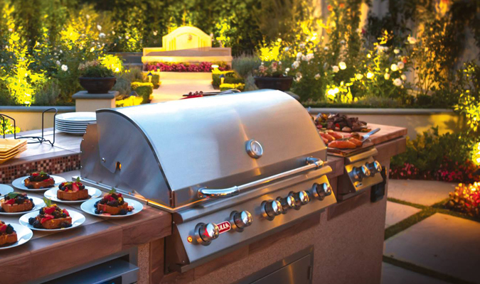 Stainless steel bull bbq grill outside on a red counter island with a light lit garden background and multiple berry deserts on both sides
