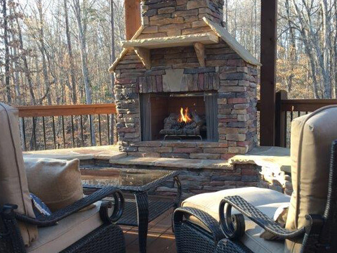 Burning outdoor fireplace with patio furniture and umbrella on a deck in Pineville, North Carolina