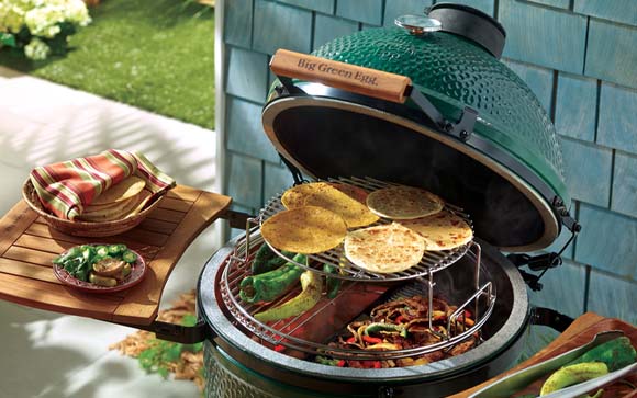 Close up capture of a Big Green Eggspander cooking fajitas and tortillas with two side wooden tables