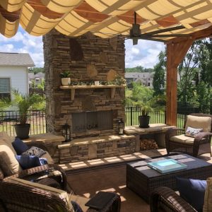 Fenced in porch with built in outdoor fireplace surrounded by wicker patio furniture