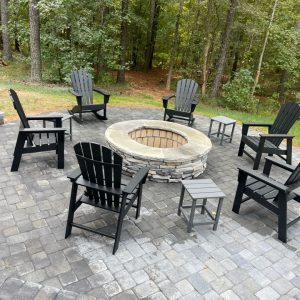 Circular fire pit with patio furniture on paved patio in backyard with trees