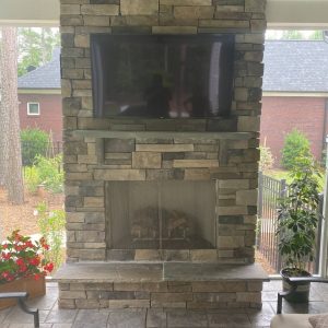 Outdoor fireplace on elevated paved patio with tv above it