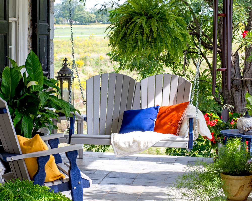 Swinging fanback chair next to other outdoor furniture on patio with green yard