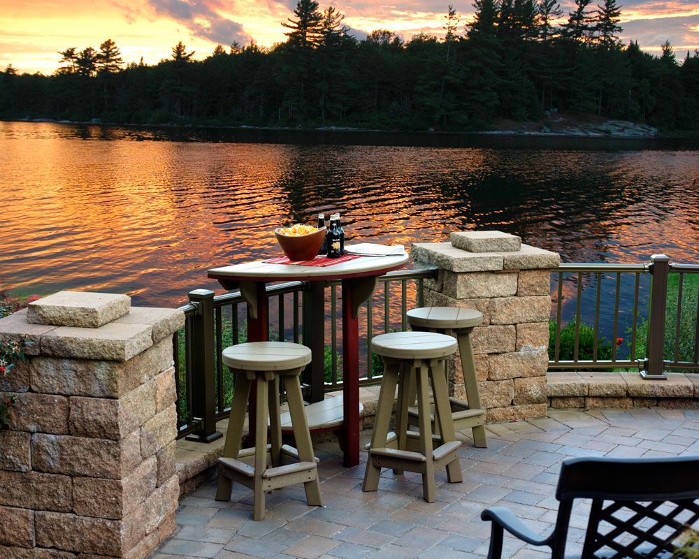 Tall table with barstools on deck next to lake during sunset