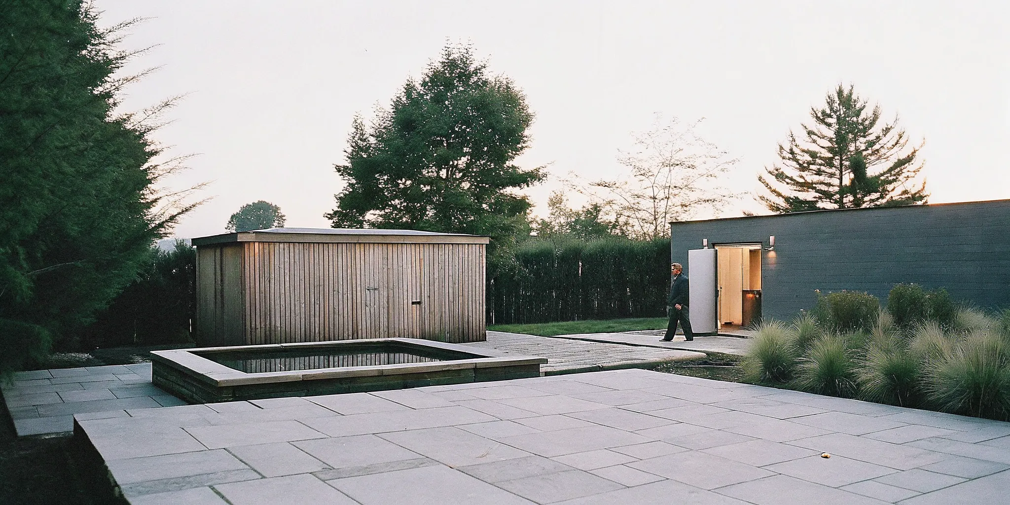 Wooden sauna and cold plunge tub in a landscaped backyard with warm evening light